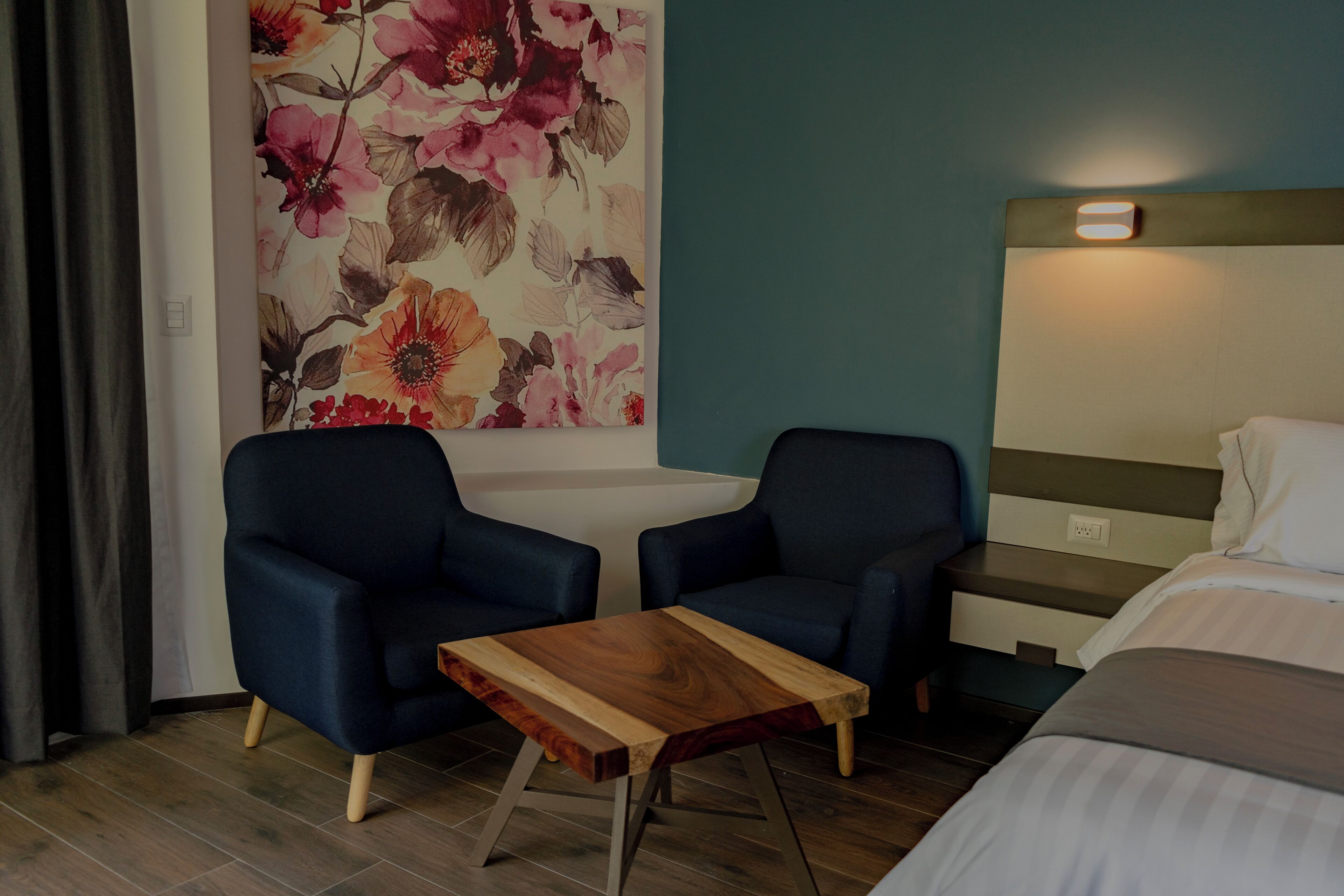 A hotel room with a bed, two armchairs, a wooden coffee table, and a floral wall decoration.