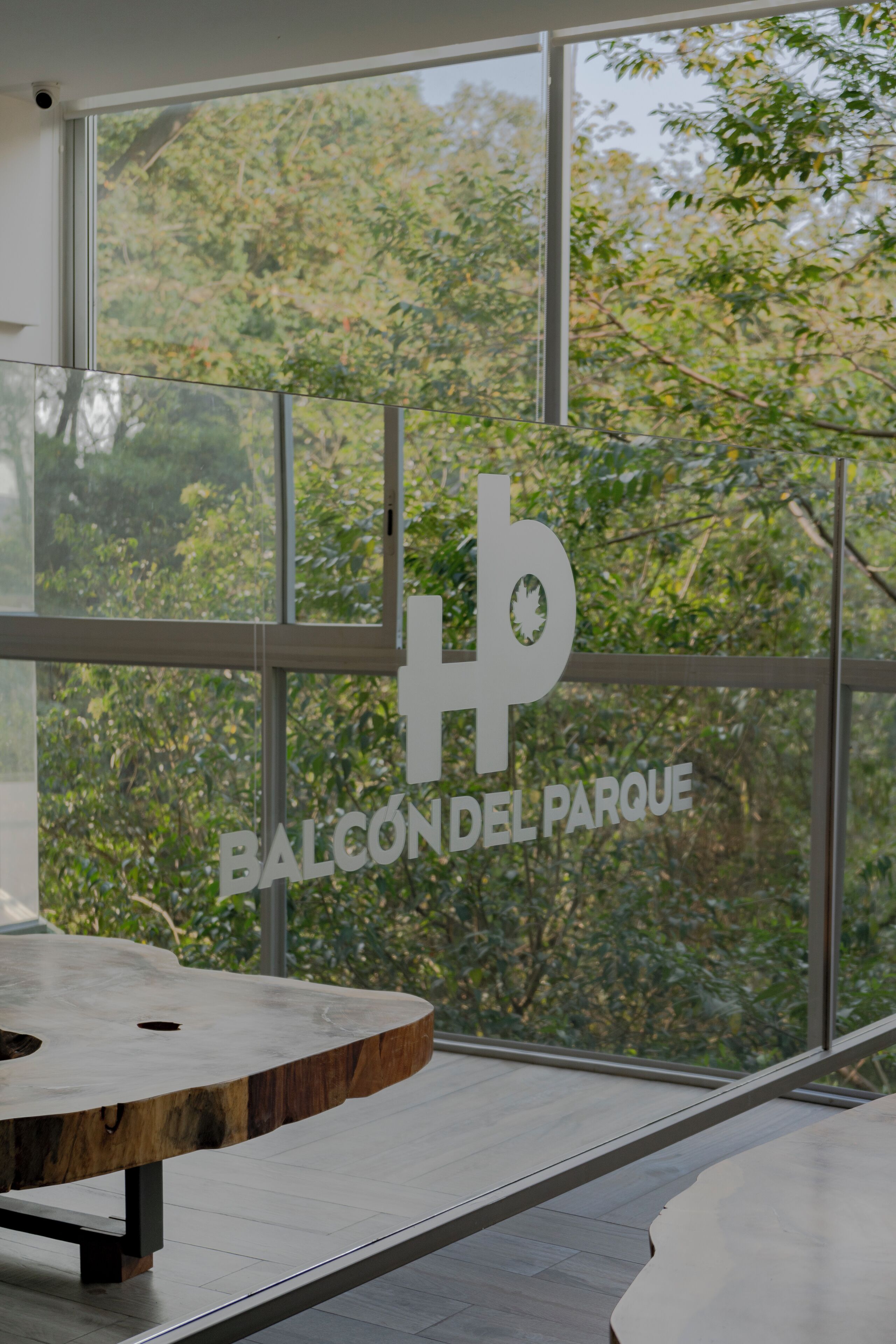 A modern interior with a large window, a wooden table, and a sign reading "BALCÓN DEL PARQUE".