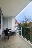 A balcony with a modern design, featuring a glass railing and a seating area with two chairs and a small table.