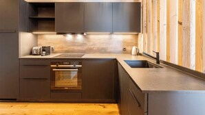 Une cuisine moderne avec des meubles de couleur sombre, un four encastré, un évier et un plan de travail sur lequel se trouve un grille-pain.