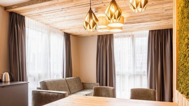 A modern dining area with a wooden table and grey upholstered chairs, a wooden ceiling, and a green wall.