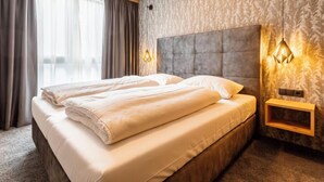 A modern hotel room with a large bed, a headboard, two bedside lamps, and a window with curtains.
