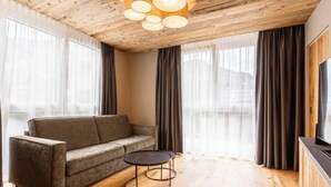 A modern living room with a wooden ceiling, a grey sofa, a round coffee table, and large windows with curtains.