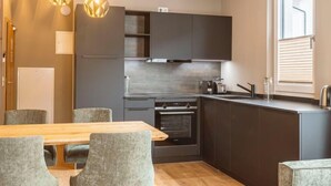 A modern kitchen with dark cabinets, a wooden dining table, and grey upholstered chairs.