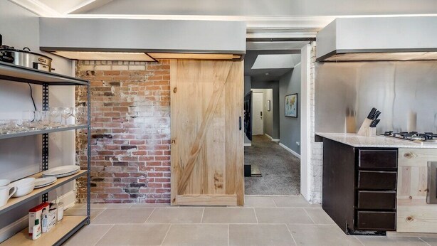 Une cuisine moderne avec un mur en briques, une porte en bois et une cuisinière en acier inoxydable.