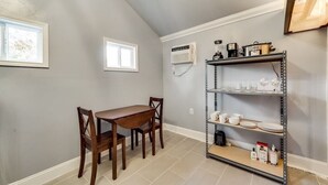 Une cuisine équipée d’une table et de chaises, d’une étagère en métal où sont rangés les ustensiles de cuisine, et d’un appareil de climatisation.