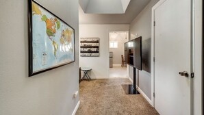 Un couloir avec une carte du monde encadrée, une petite table et un téléviseur sur le côté droit.