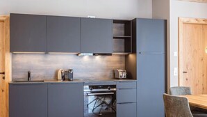 Una cocina moderna con armarios oscuros, horno empotrado y comedor con mesa y sillas de madera.