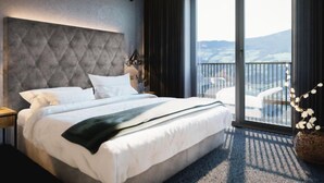 Ein modernes Hotelzimmer mit einem großen Bett, Blick ins Freie durch eine Schiebetür und einem Balkon mit Sitzgelegenheit.