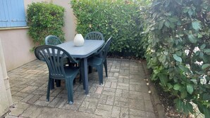A patio with a table and chairs, surrounded by greenery and a building in the background. - Centrally located apartment with swimming pool (Fréjus)