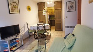 A living room with a TV, a glass coffee table, a sofa, and a dining area with chairs and a table. - Centrally located apartment with swimming pool (Fréjus)