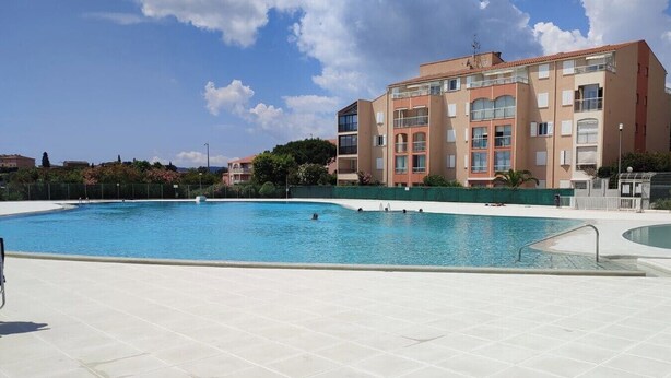A swimming pool with a tiled deck, surrounded by apartment buildings. - Centrally located apartment with swimming pool (Fréjus)
