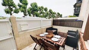 An outdoor patio with a wooden table set for dining, surrounded by chairs and a cushioned bench. - Cosy Town house with its beautiful terrace (Deauville)
