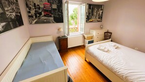A bedroom with two beds, a window with a view of greenery, and two black and white cityscape posters on the walls. - Cosy Town house with its beautiful terrace (Deauville)