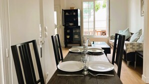A dining area with a dark wooden table set for four, white plates, and clear glasses. A black cabinet with glassware is in the background. - Cosy Town house with its beautiful terrace (Deauville)