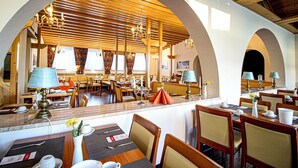 Un restaurante con vigas de madera, techos abovedados y una zona central de comedor con mesas y sillas.