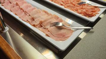 Un bufé con diversos tipos de carne y un tenedor sobre una bandeja.