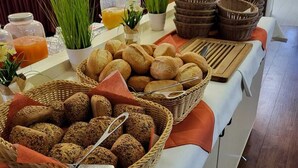 A buffet table with various breads and pastries, a juice dispenser, and decorative plants. - Morada Hotel Bad Wörishofen (Bad Woerishofen)