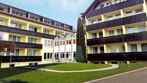 Un hotel de varios pisos con una fachada simétrica, balcones y un patio central con un árbol alto y cónico.