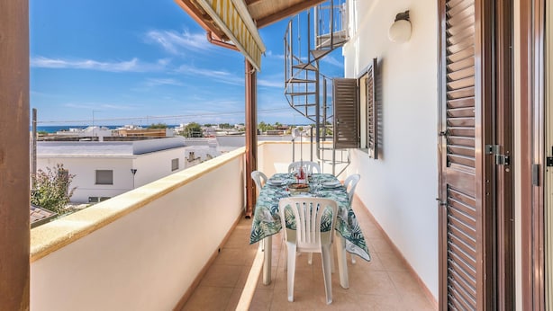 Een balkon met een tafel en stoelen, een wenteltrap en uitzicht op de stad.