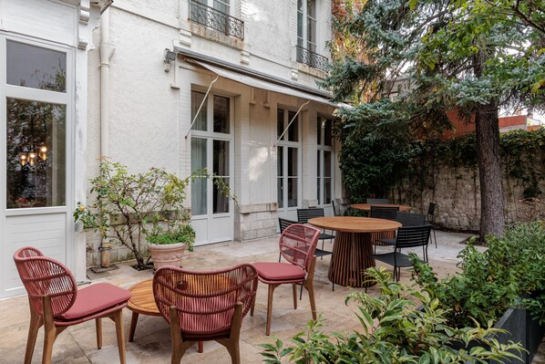 A patio with wicker chairs and a round table, surrounded by potted plants and a stone wall. - Frenchdoor Orléans Arago (Orléans)