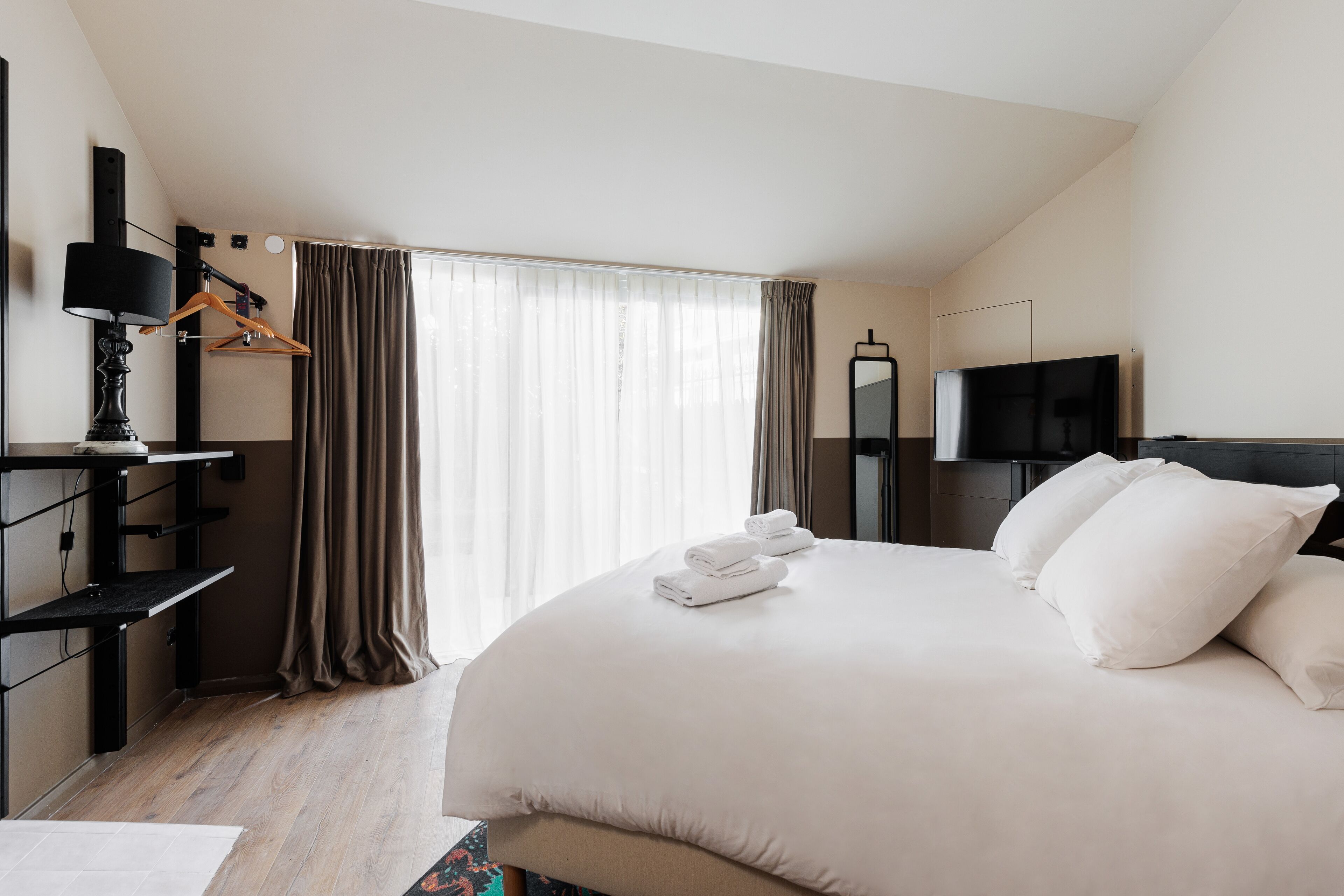 Quarto de hotel moderno com uma cama grande, televisão de tela plana, escrivaninha com luminária e um guarda-roupa.
