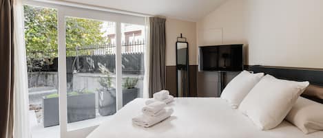 Habitación de hotel con una cama grande, televisión y vistas a un jardín a través de una puerta corredera.