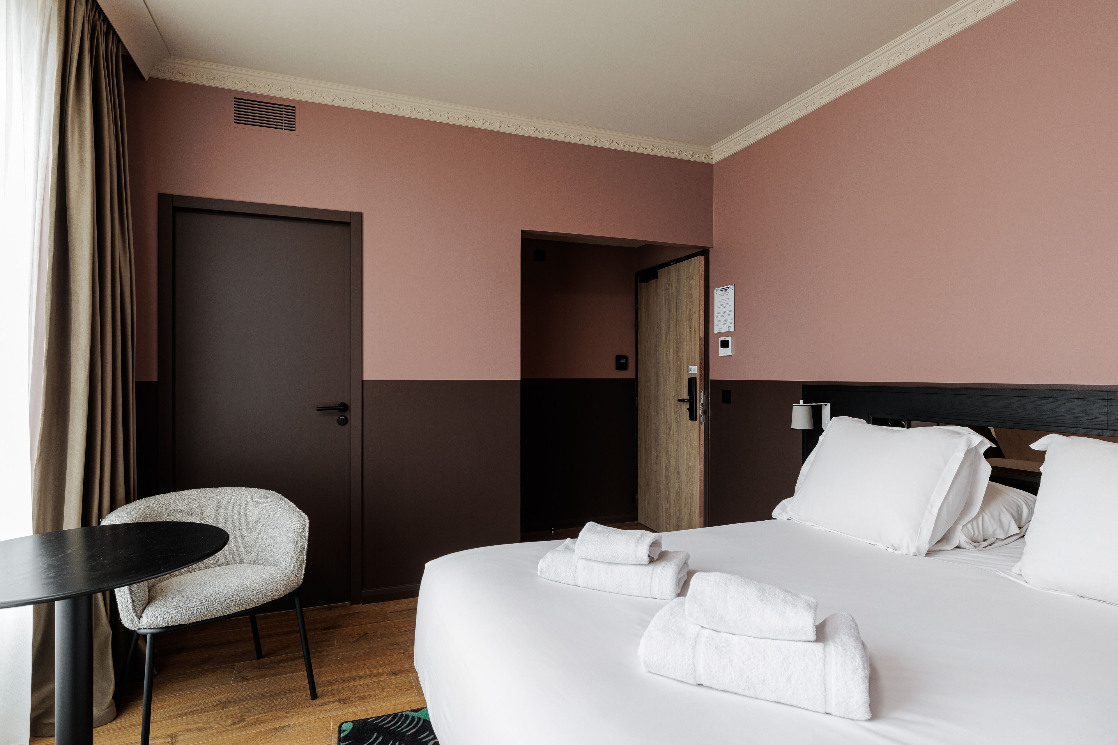 A hotel room with a large bed, a chair, a desk, and a door.