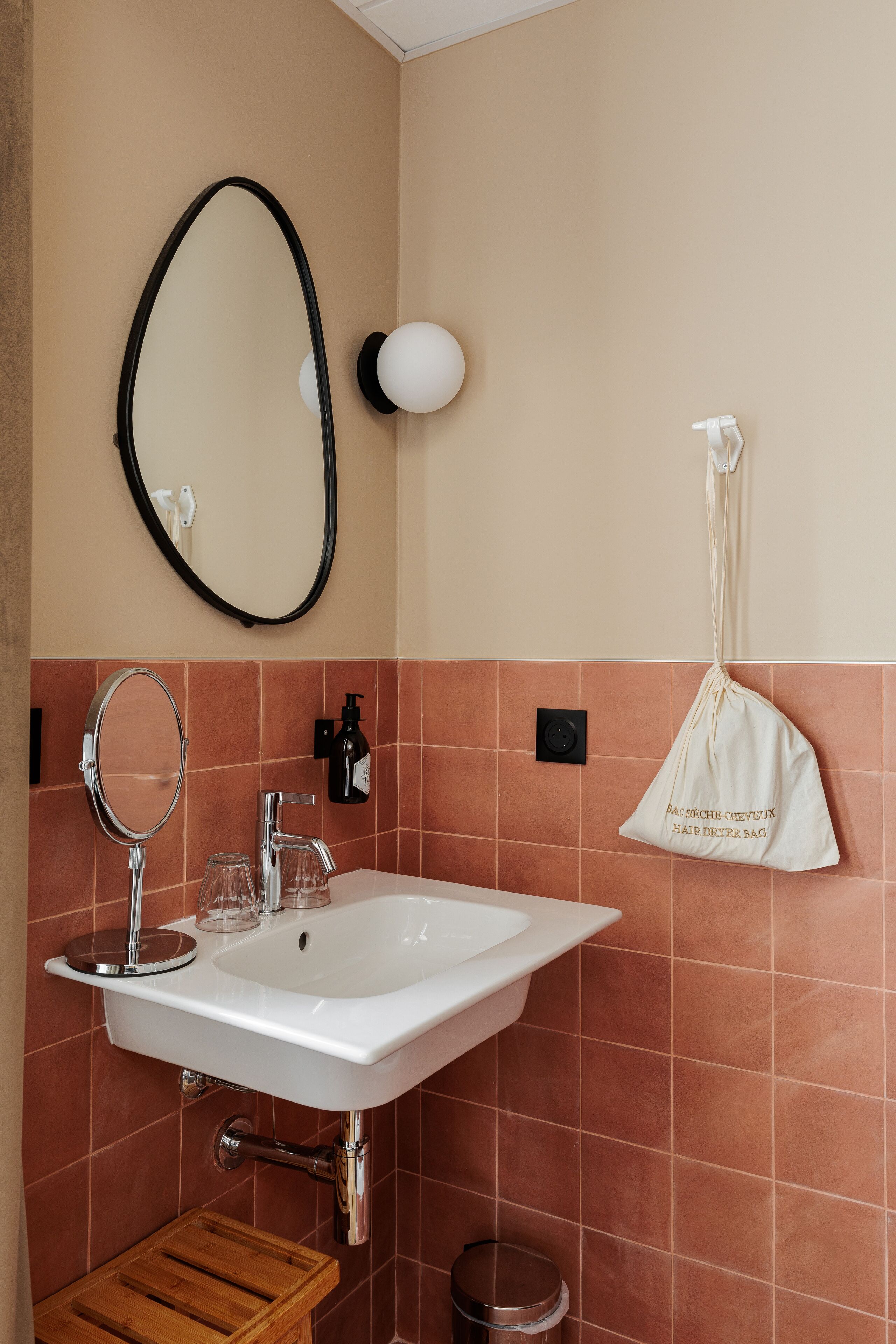 Een badkamer met een witte wastafel, een ronde spiegel en een hangende tas met tekst.