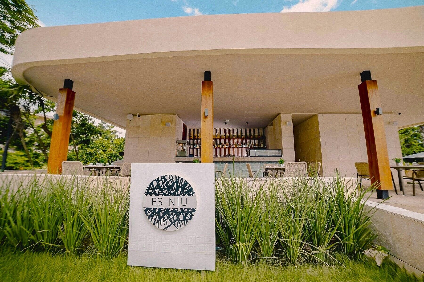 An outdoor seating area with a modern design, featuring a large circular sign with the text "ES NIU" and a geometric pattern.