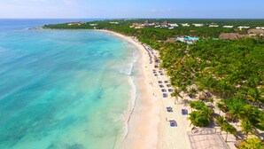 Un resort en la playa con orilla arenosa, palmeras y mar azul cristalino.