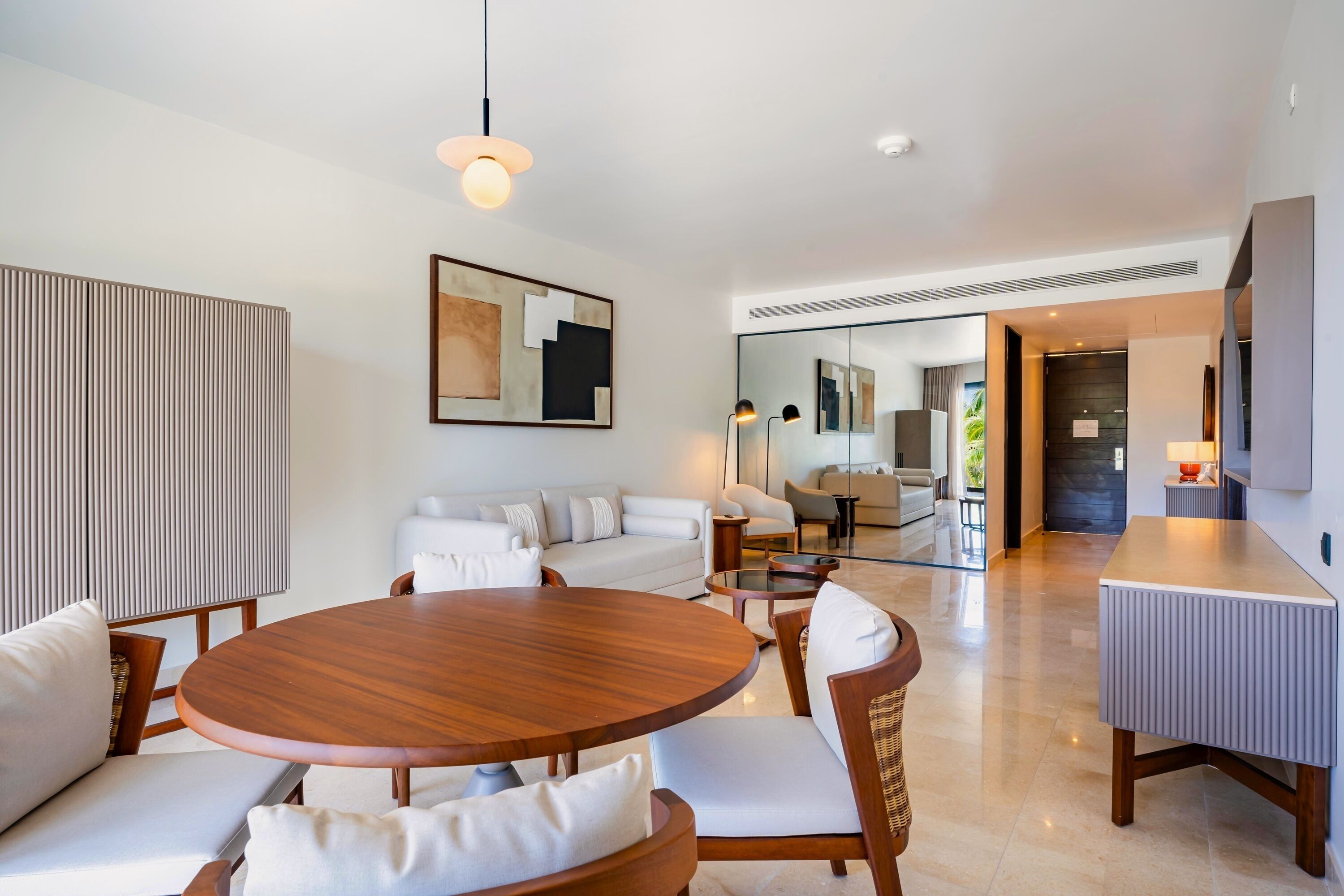 Una sala de estar moderna con una mesa redonda de madera, sofás blancos y un espejo grande.