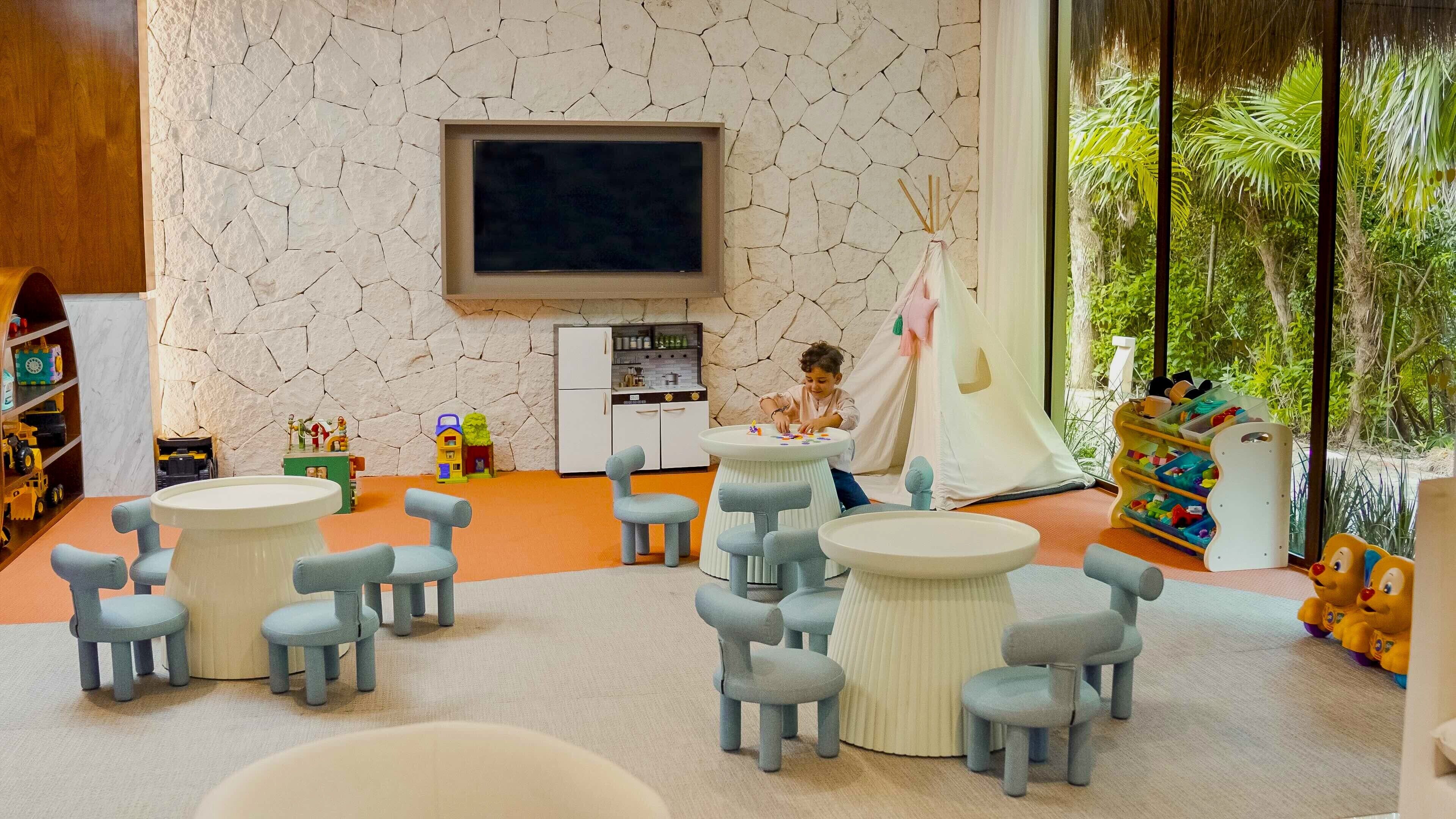 A children's playroom with a stone wall, a television, and a large window with a view of greenery.