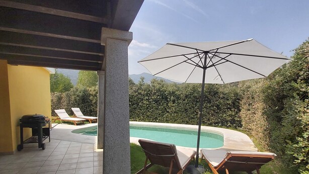 En overdækket terrasse med en pool, to liggestole og en parasol.