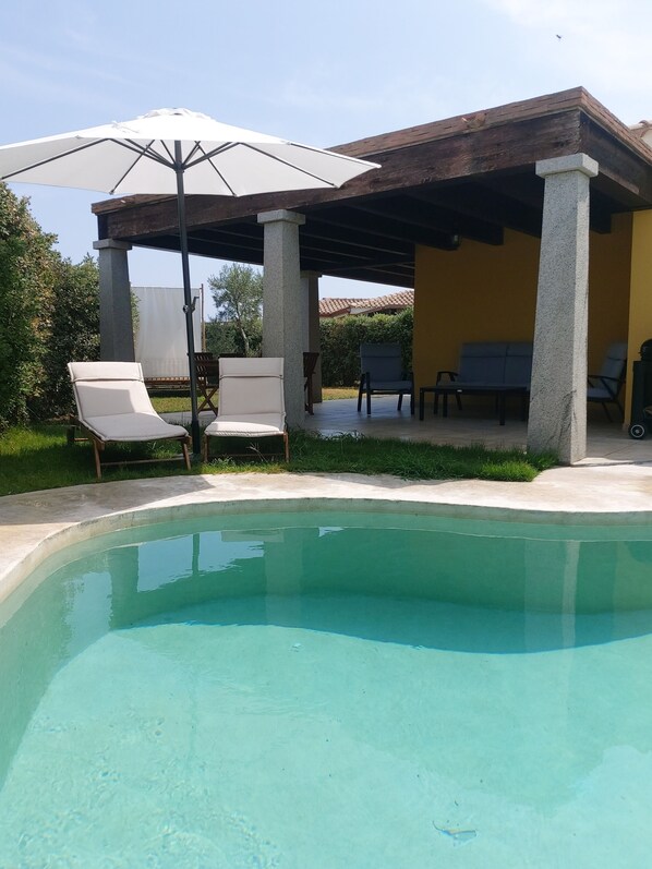 A pool area with lounge chairs and a covered seating area.