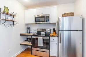 Compact kitchen with stainless steel appliances, oven, and microwave, featuring a coffee maker and ample storage.