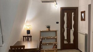 A dining area with a table and chairs, a small shelf with decorative lights, and a door with a unique design.