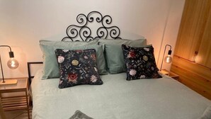 A neatly made bed with floral pillows, a grey blanket, and folded towels on a wooden headboard.