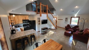 A spacious living area with a kitchen, a wooden dining table, and a staircase leading to an upper level. - Brightstone Lake Cabin 1 (Union Township)