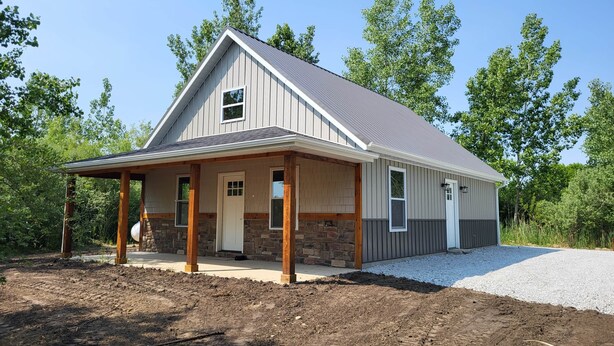 A single-story house with a gabled roof, a covered porch, and a stone foundation. - Brightstone Lake Cabin 1 (Union Township)