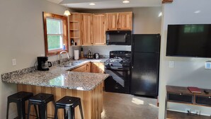 A kitchen with granite countertops, wooden cabinets, a black refrigerator, a microwave, a stove, and a window with a view of greenery. - Brightstone Lake Cabin 1 (Union Township)