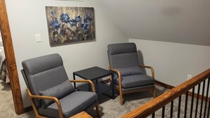 A room with two grey armchairs and a small black table, a wooden staircase, and a painting of blue flowers on the wall. - Brightstone Lake Cabin 1 (Union Township)