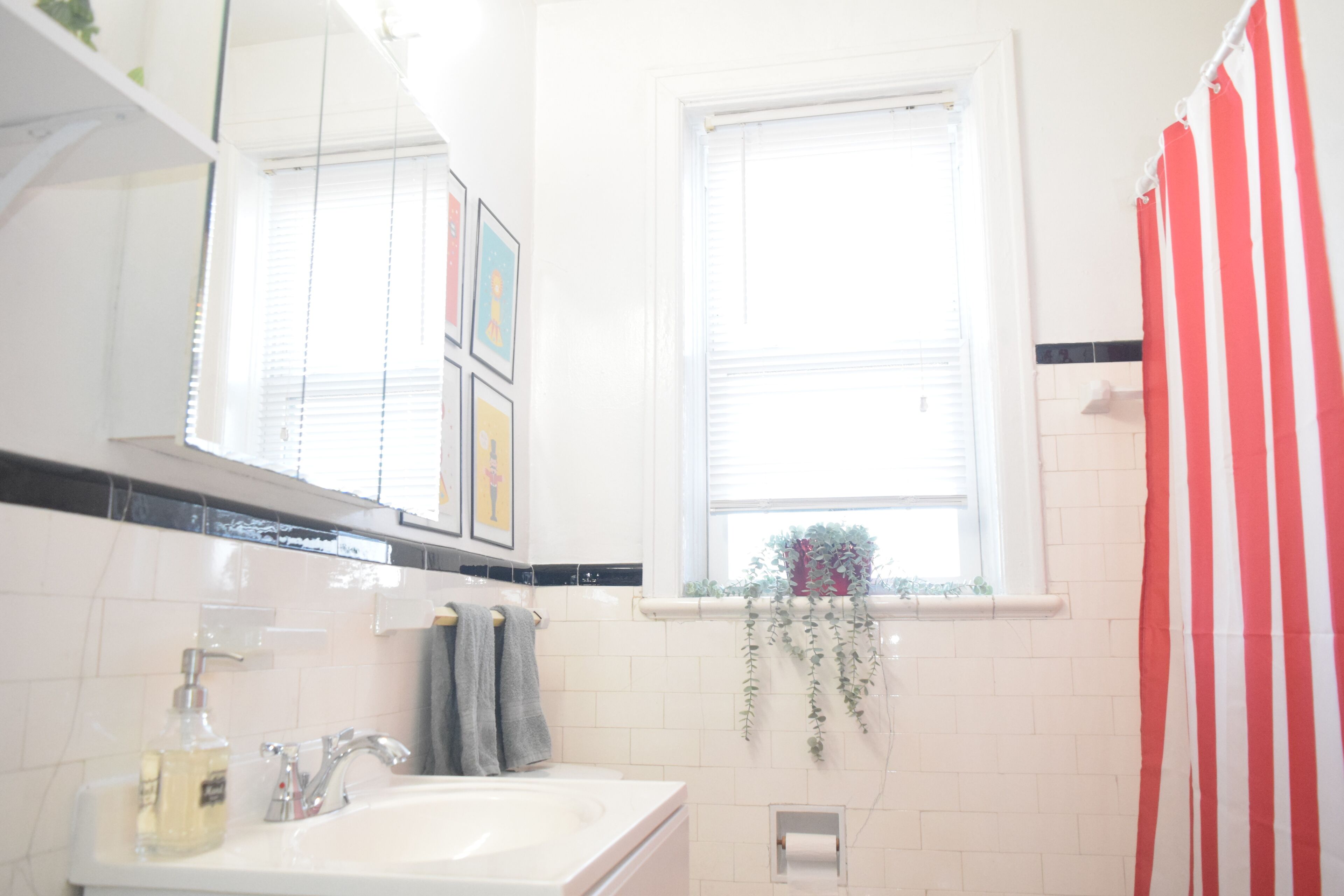 A bathroom with a white sink, a mirror, a window with a view, and a red and white striped shower curtain.