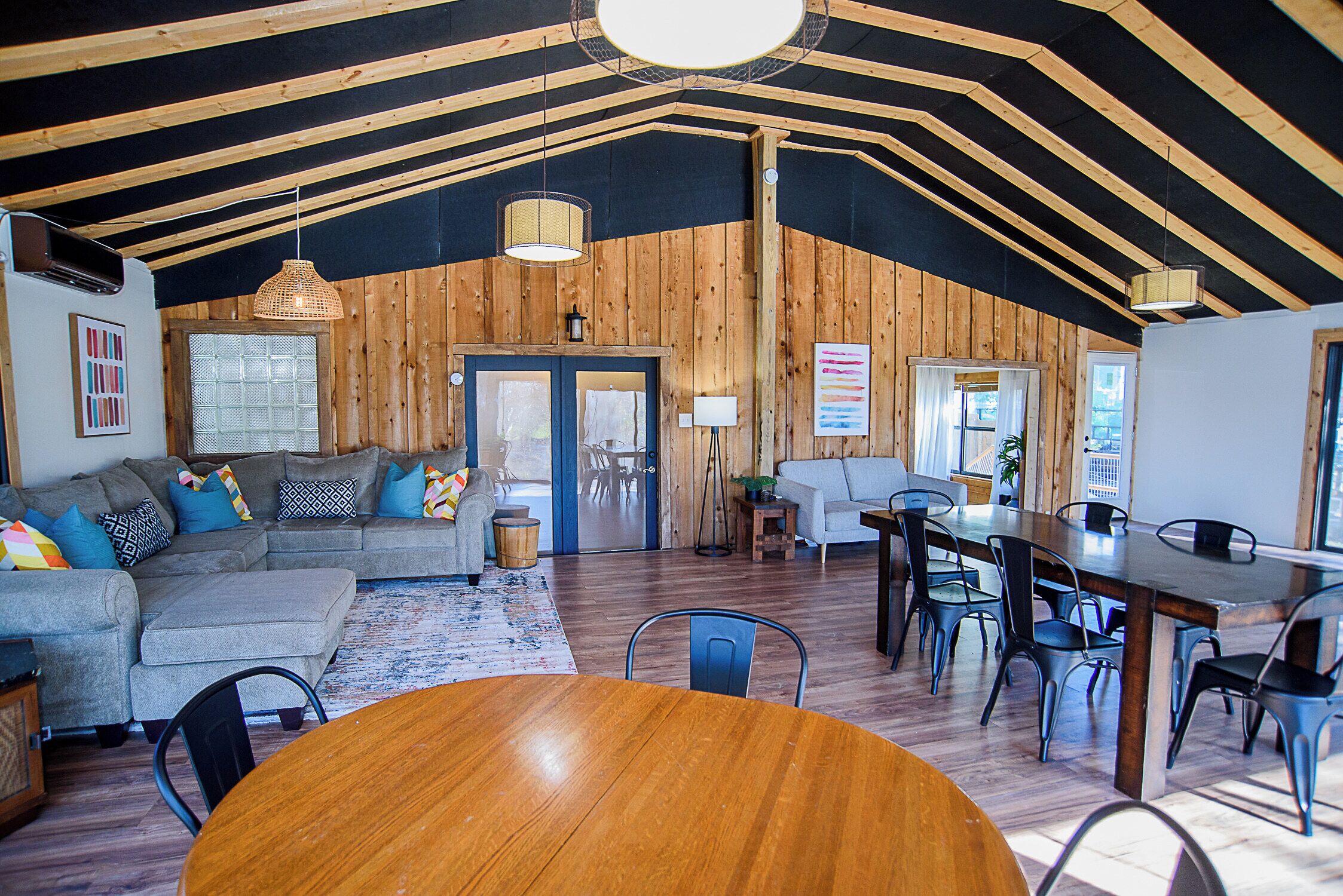 A spacious loft with a high ceiling, wooden walls, a dining area with a round table, and a living area with a sofa and chairs.