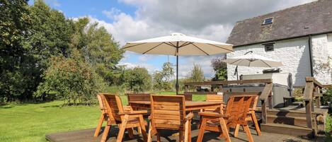 A wooden deck with a table and chairs, a hot tub, and a stone building in the background.