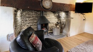 A cozy living room with a stone fireplace, a leather sofa with a plaid pillow, and a flat-screen TV mounted on the wall. - Penarth (Llandrindod Wells)