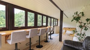 A modern bar area with a long counter, multiple bar stools, and large windows offering a view of the outdoors. - Penarth (Llandrindod Wells)