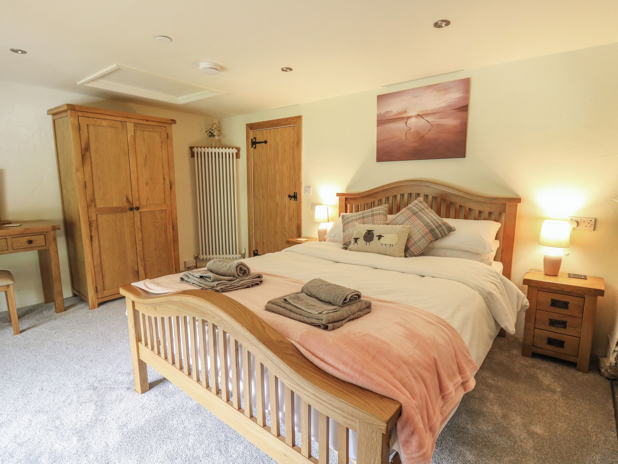 A bedroom with a wooden bed, bedside tables, a radiator, and a painting on the wall.