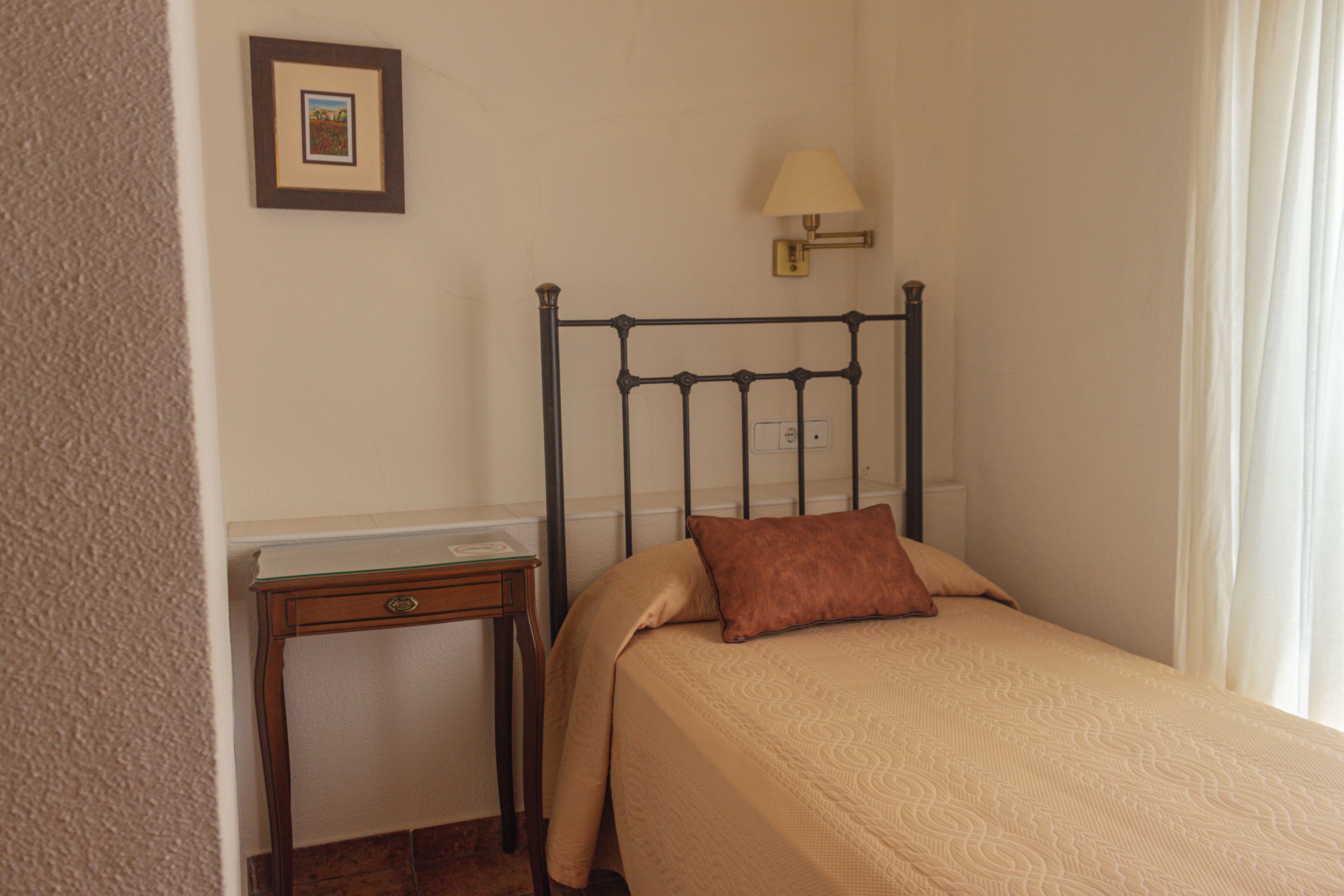 Een slaapkamer met een bed, nachtkastje, lamp en een ingelijste foto aan de muur.