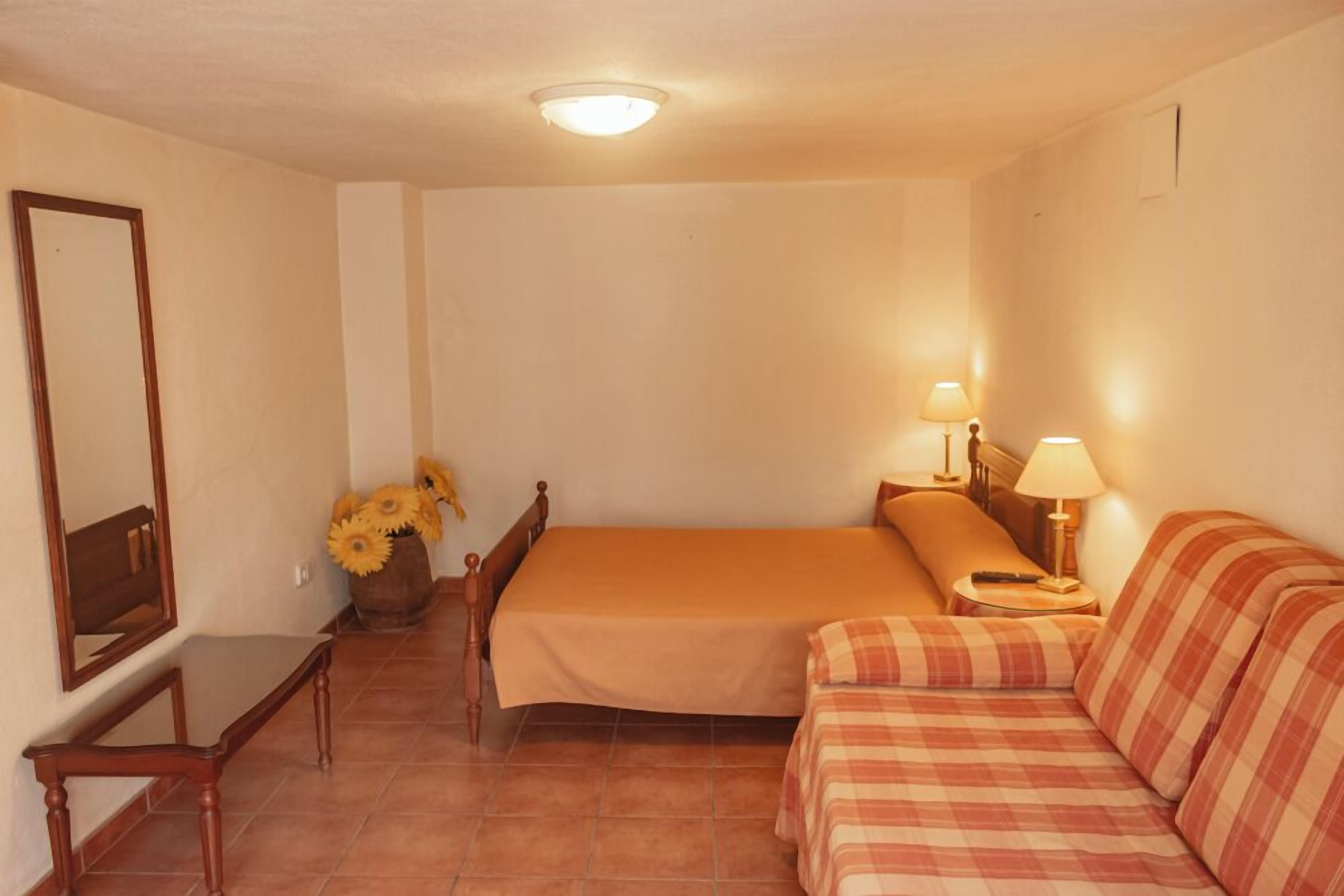 Une chambre à coucher avec un lit, un canapé, une table de chevet, une lampe, un miroir et un vase rempli de tournesols.